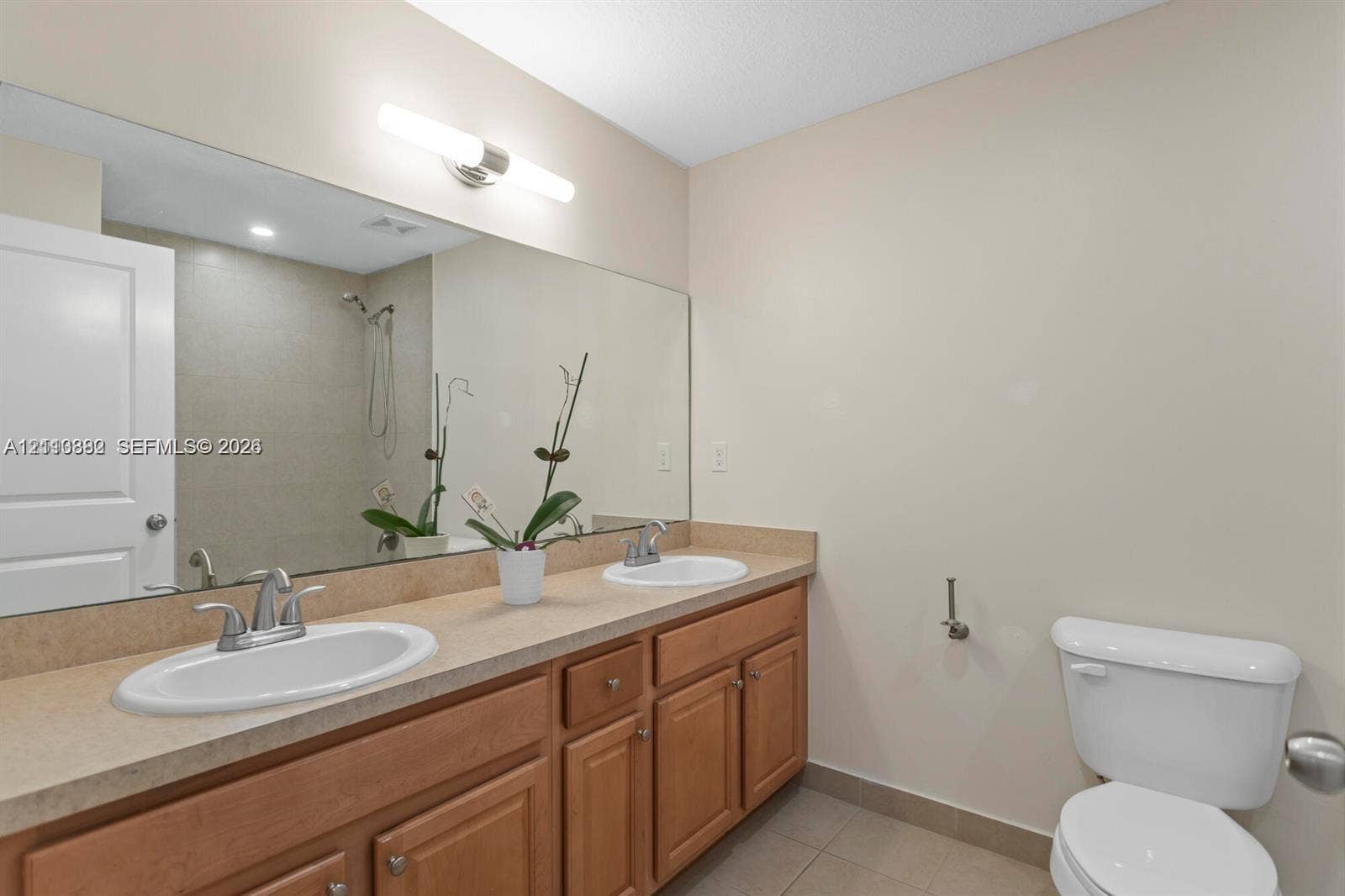 Double vanity featuring solid-surface countertops, dual drop-in sinks with chrome hardware, wood cabinetry, and a full-width wall mirror
