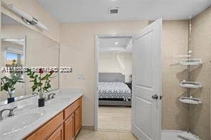 Dual-sink vanity with light wood-finish cabinetry, solid-surface countertop, full-width vanity mirror, and neutral wall tile surround in the shower area