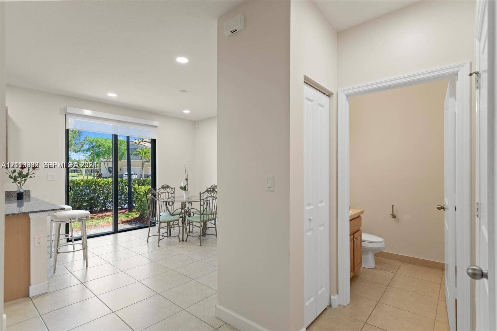 Ceramic tile flooring, recessed lighting, breakfast bar with stone-surface countertop, floor-to-ceiling glass sliding doors, and bi-fold closet doors