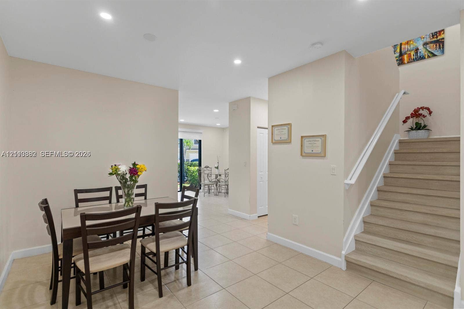 Neutral-toned interior space featuring light-colored tile flooring, recessed ceiling lighting, a staircase with wood-finish treads, and a white handrail