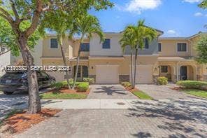 Two-story exterior featuring a paver driveway, attached garage, and multi-tone stucco facade with palm tree landscaping