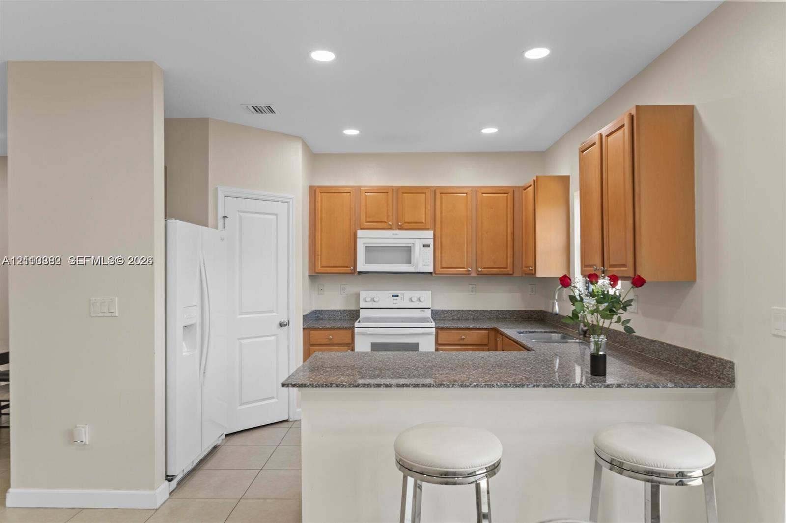 Kitchen featuring wood cabinetry, stone-finish countertops, recessed lighting, tile flooring, and white kitchen appliances