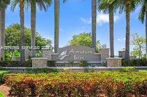 Community entrance signage featuring masonry pillar accents, decorative landscaping, and mature palm trees