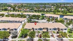 Aerial perspective of a multi-unit residential property featuring a tiled roof, light-toned exterior siding, and paved driveways, situated near a waterway and landscaped green spaces