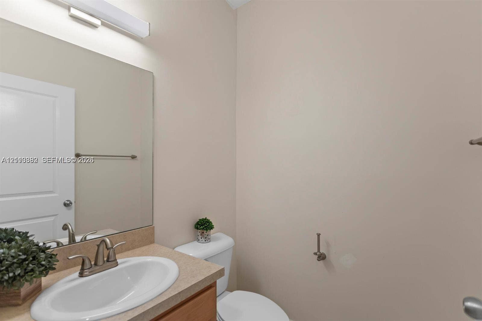 Neutral-toned bathroom featuring a surface-mounted sink, wide vanity mirror, metallic finish fixtures, and a wall-mounted light bar