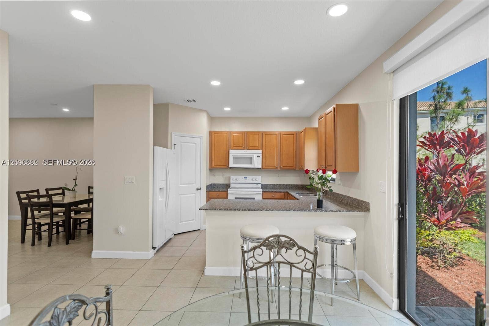 Kitchen featuring natural wood-finish cabinetry, stone-style countertops, a breakfast bar, recessed lighting, and tile flooring