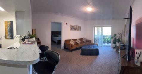 200 SW 117th Terrace, #10103, Pembroke Pines, FL 33025 Living area featuring neutral carpeting, a stone-patterned breakfast bar, and glass sliding doors providing exterior access