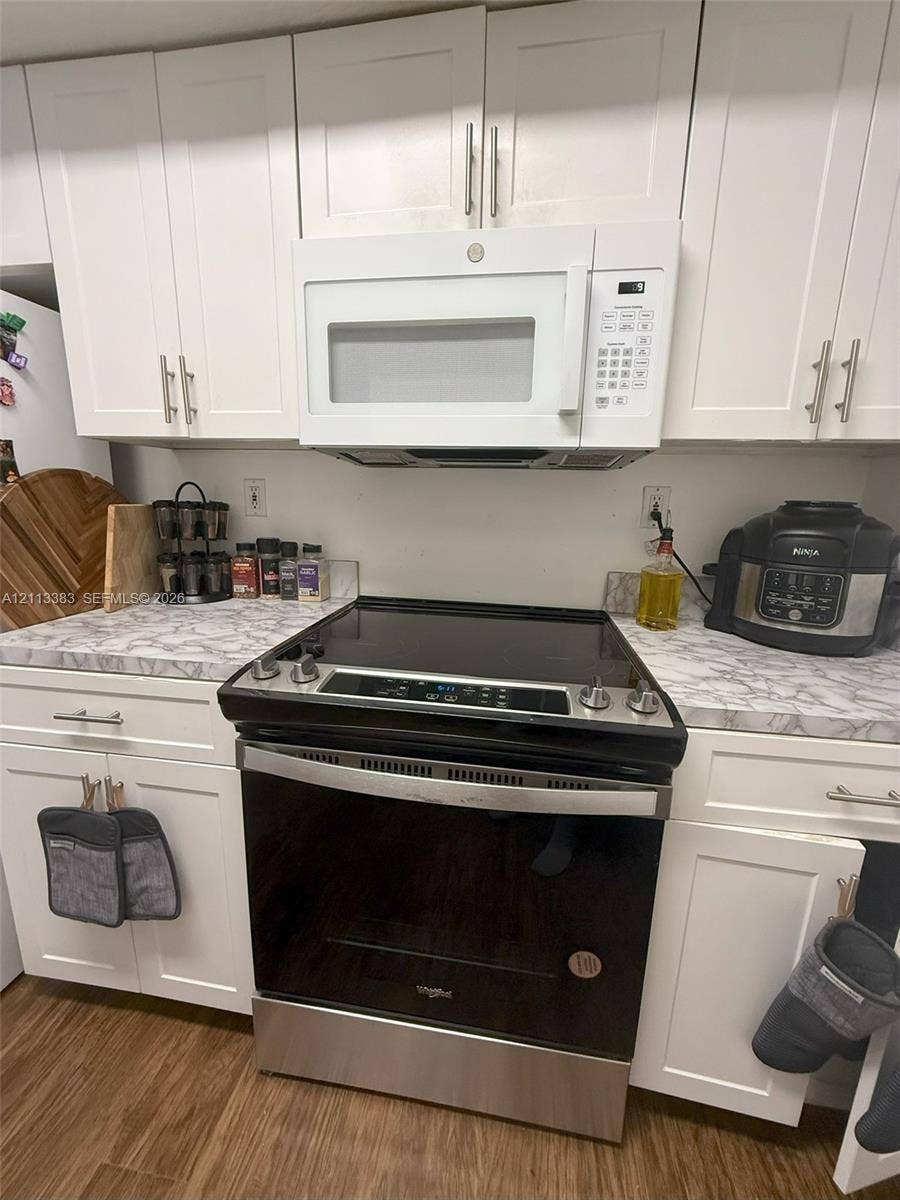 200 SW 117th Terrace, #10103, Pembroke Pines, FL 33025 Kitchen featuring white Shaker-style cabinetry, stone-patterned laminate countertops, stainless steel electric slide-in range, matching over-the-range microwave, and wood-finish flooring