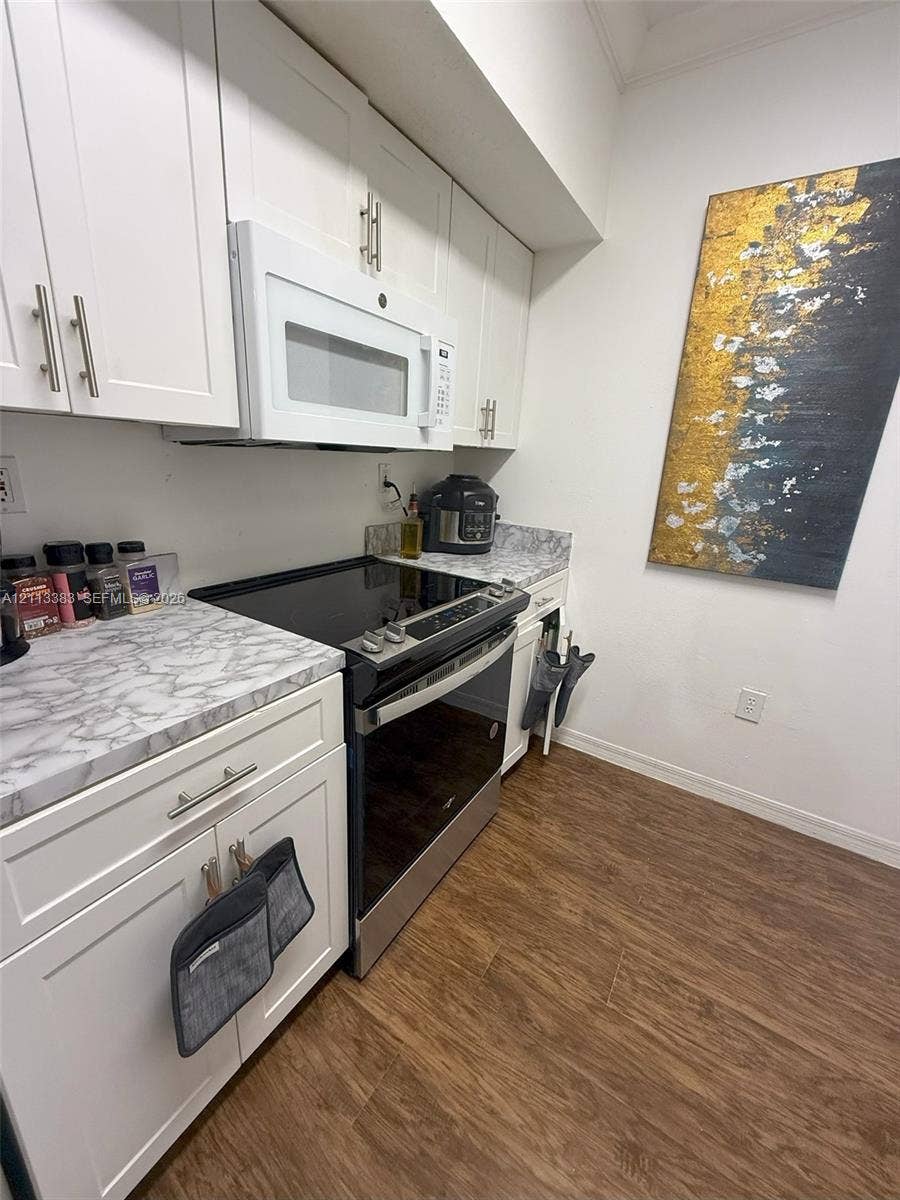 200 SW 117th Terrace, #10103, Pembroke Pines, FL 33025 Kitchen featuring white cabinetry, stone-patterned laminate countertops, integrated over-the-range microwave, smooth-top electric range, and wood-finish flooring
