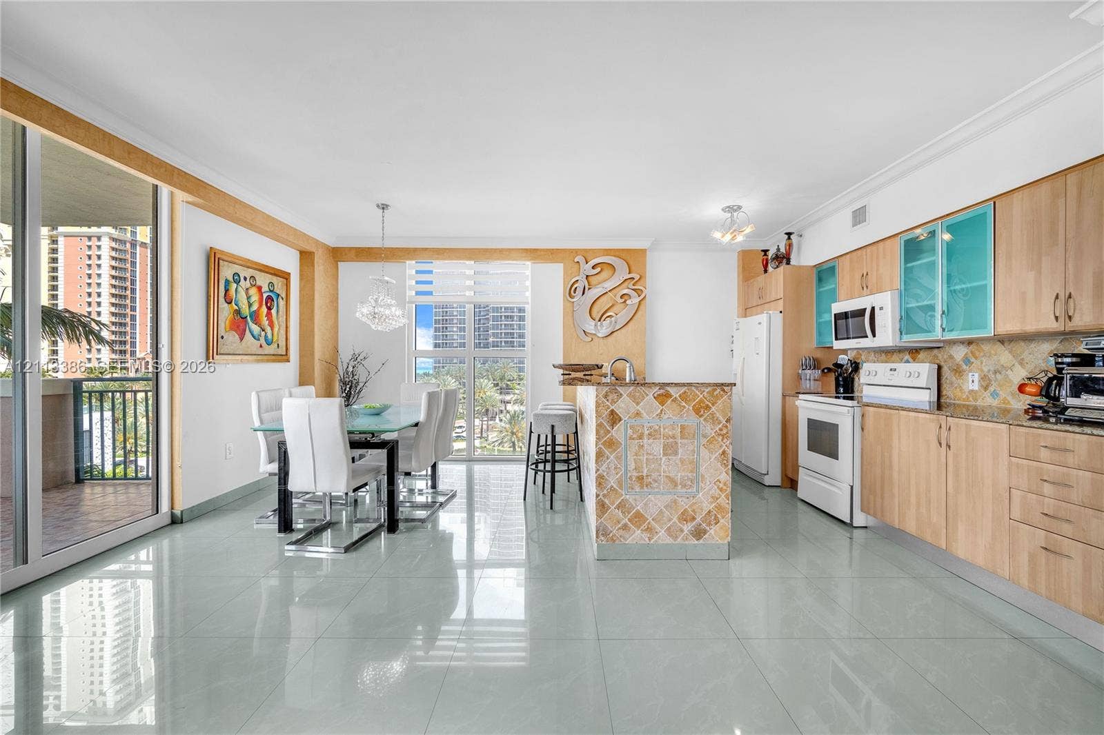 Open-concept area featuring light wood-finish cabinetry, tile-clad kitchen island, polished tile flooring, glass-paneled upper cabinets, and floor-to-ceiling glass sliding doors