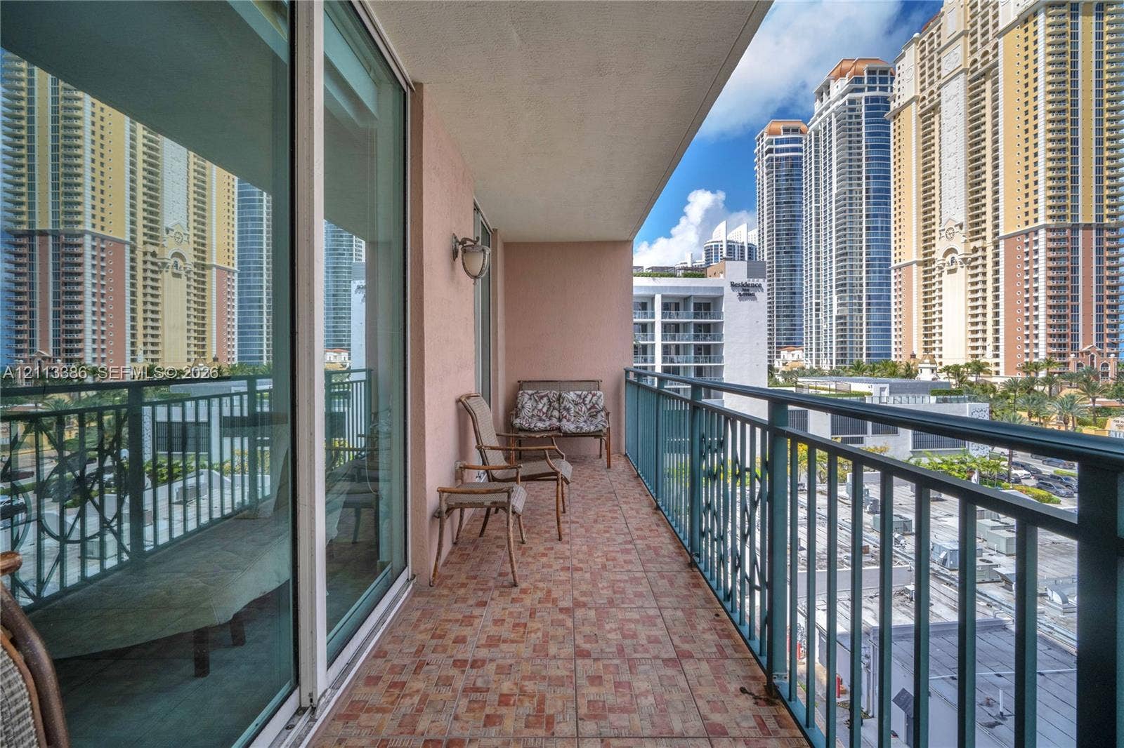 Covered balcony featuring patterned tile flooring, a wall-mounted light fixture, and a metal railing