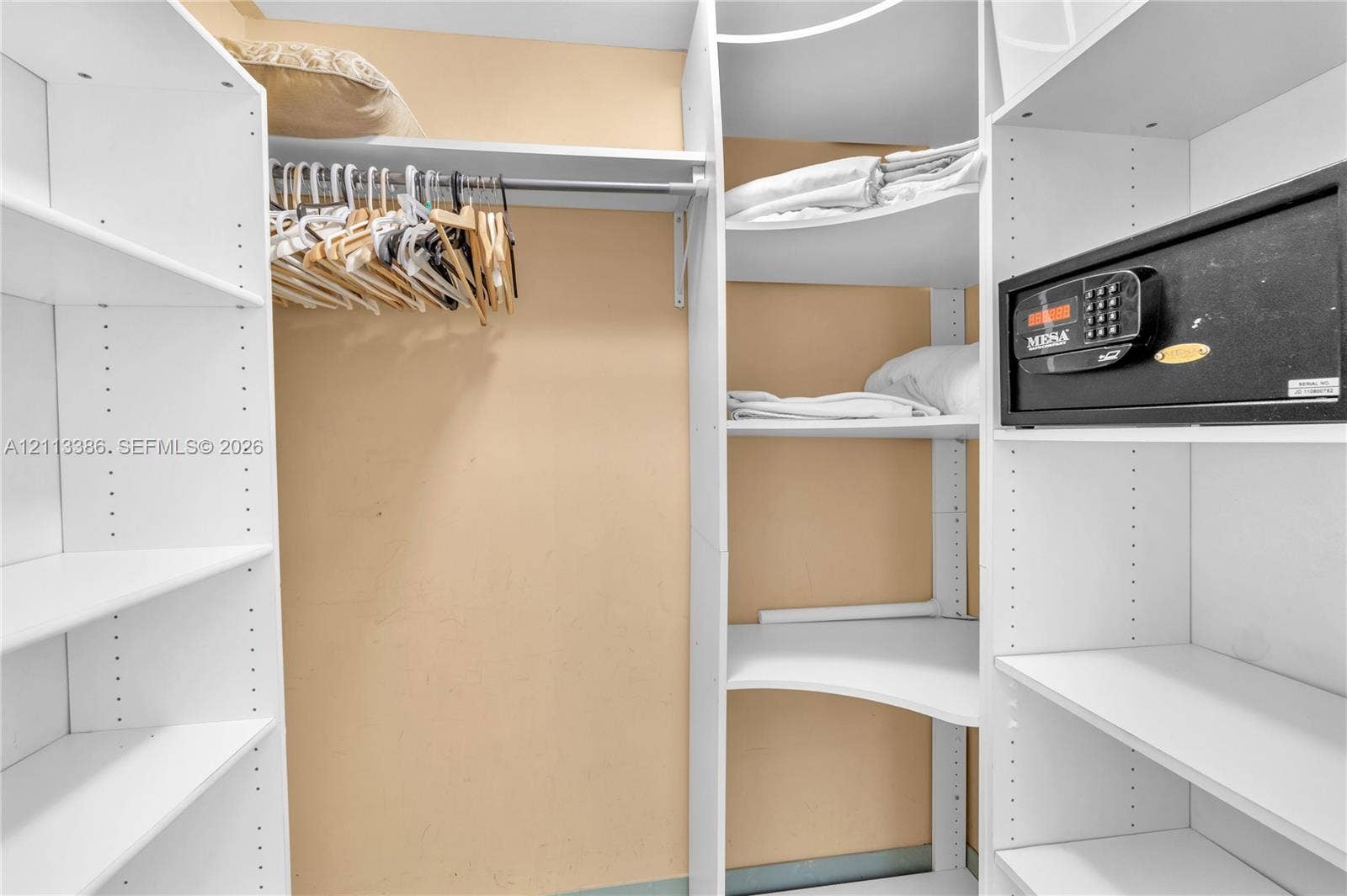 Walk-in closet featuring white floor-to-ceiling built-in shelving, adjustable storage cubbies, a hanging rod, and a built-in security safe