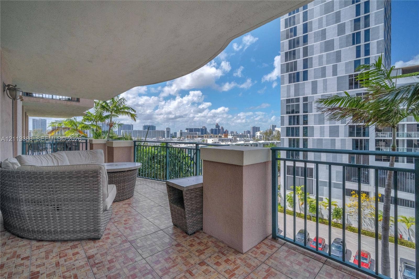 Covered balcony featuring tiled flooring, a solid concrete overhang, and dark metal railings with urban surroundings