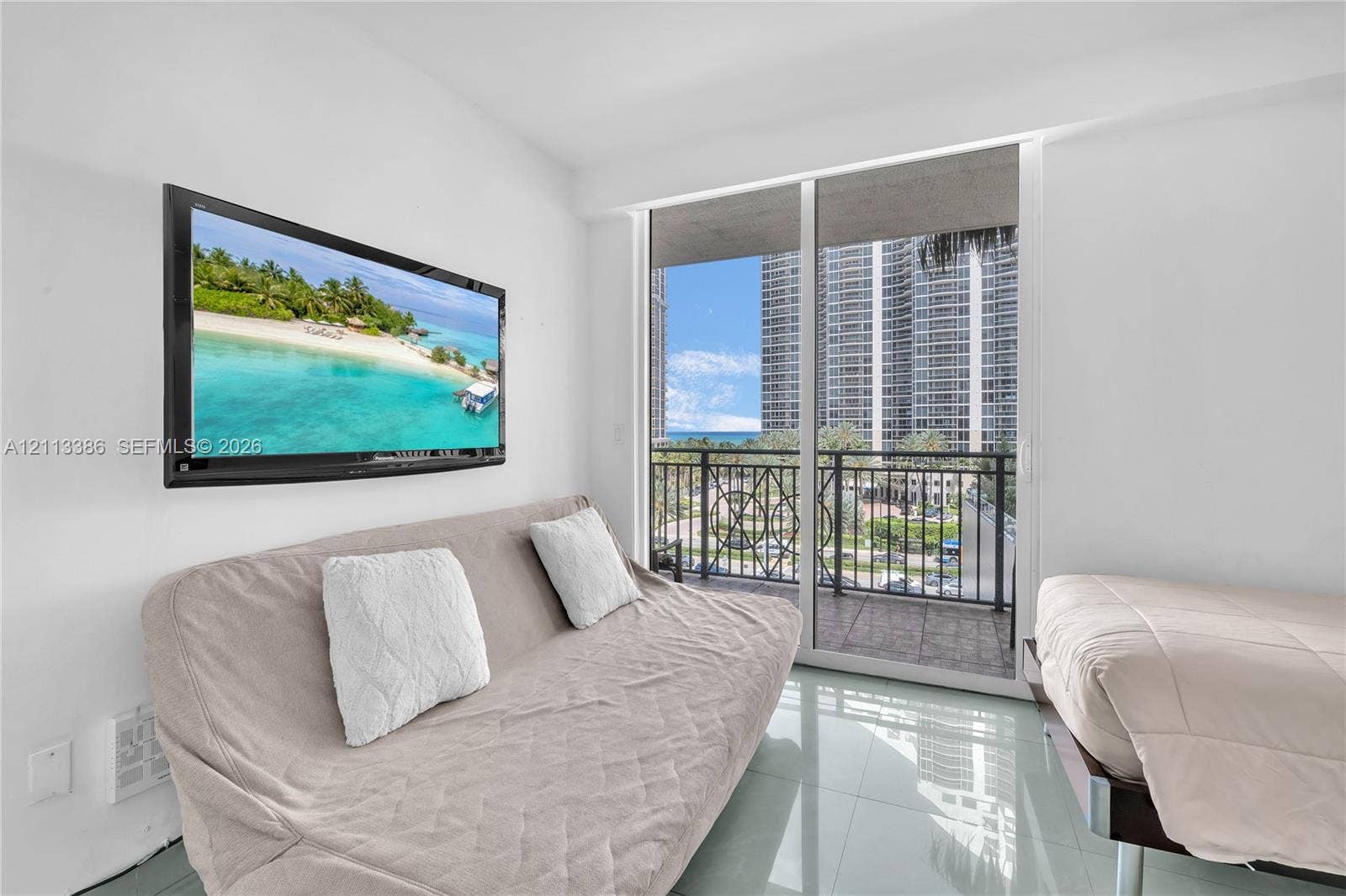 Sliding glass door opening to a private balcony with metal railing, reflective tile flooring, and wall-mounted television