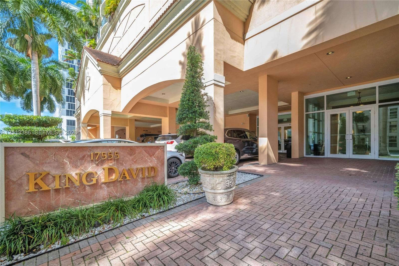 Covered porte-cochre entry featuring a red brick paver driveway, natural stone monument signage, and structured landscape elements