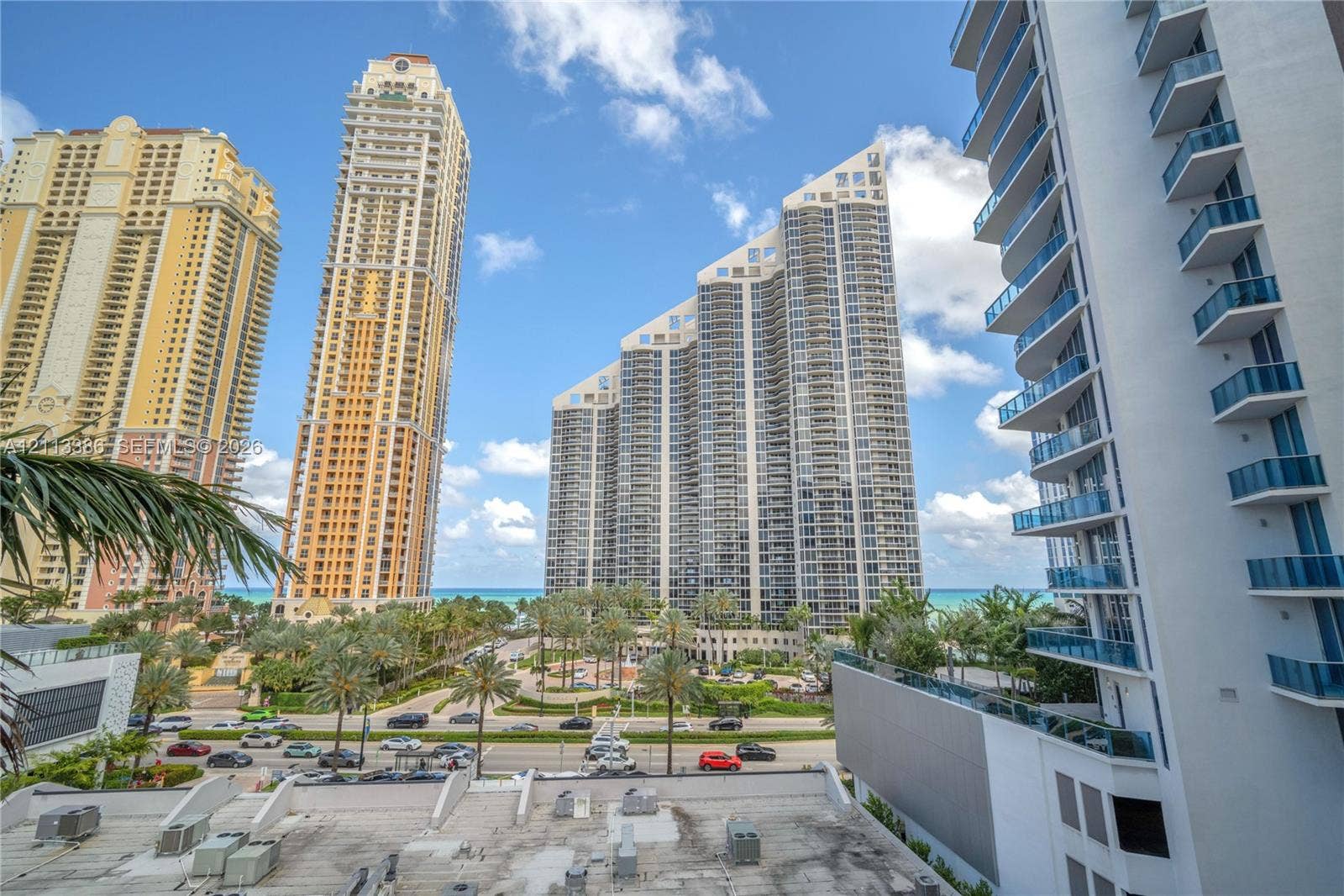 High-rise exterior featuring stacked glass-railing balconies and architectural building facades set against a coastal backdrop