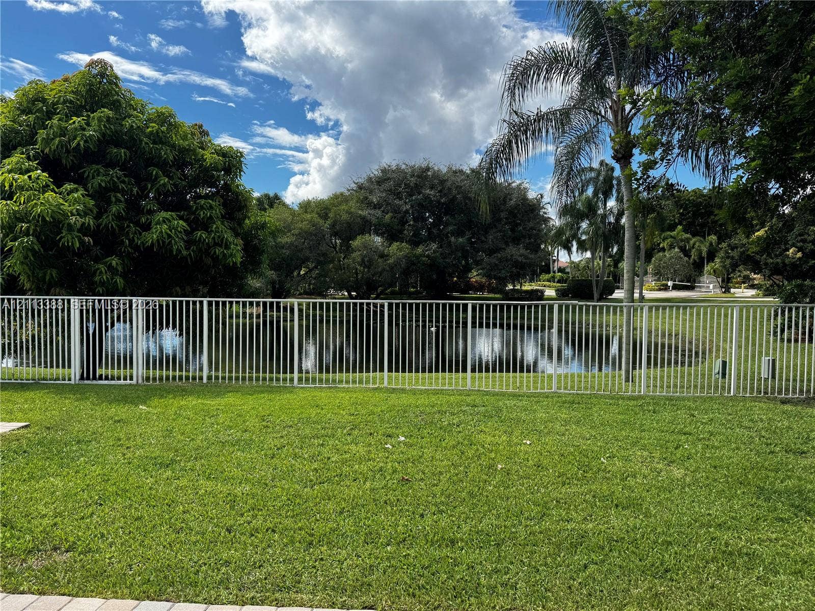 527 Water Point, Weston, FL 33326 Outdoor space featuring a manicured lawn, white metal fencing, mature trees, and a pond
