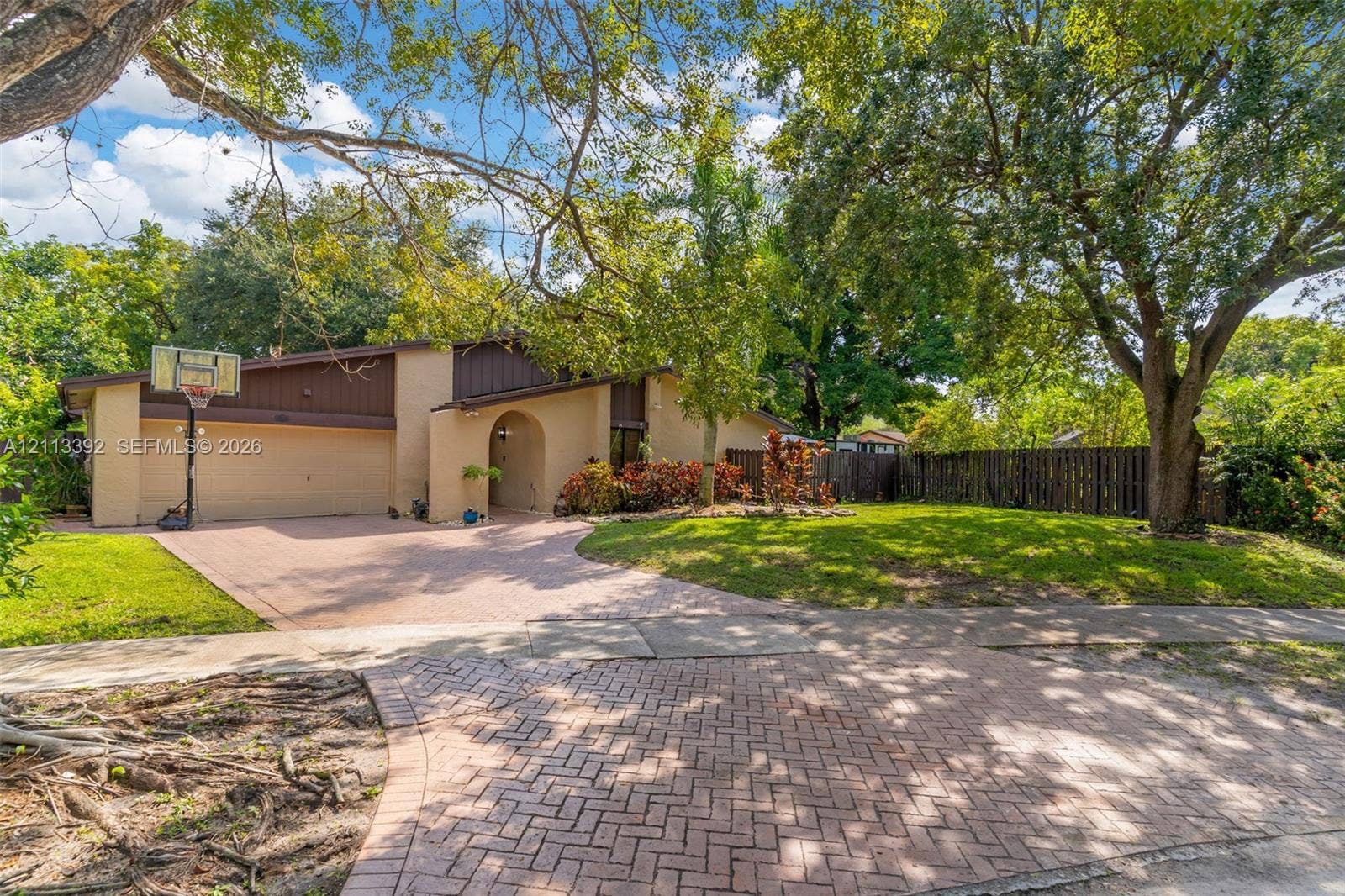 10705 SW 134th Court, Miami, FL 33186 Exterior elevation featuring a multi-tonal facade, paved brick driveway, attached two-car garage, mature landscaping, and fenced perimeter