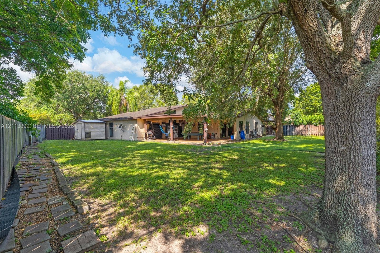 10705 SW 134th Court, Miami, FL 33186 Expansive backyard featuring a covered patio, mature canopy trees, a grass lawn, and stone paver walkway