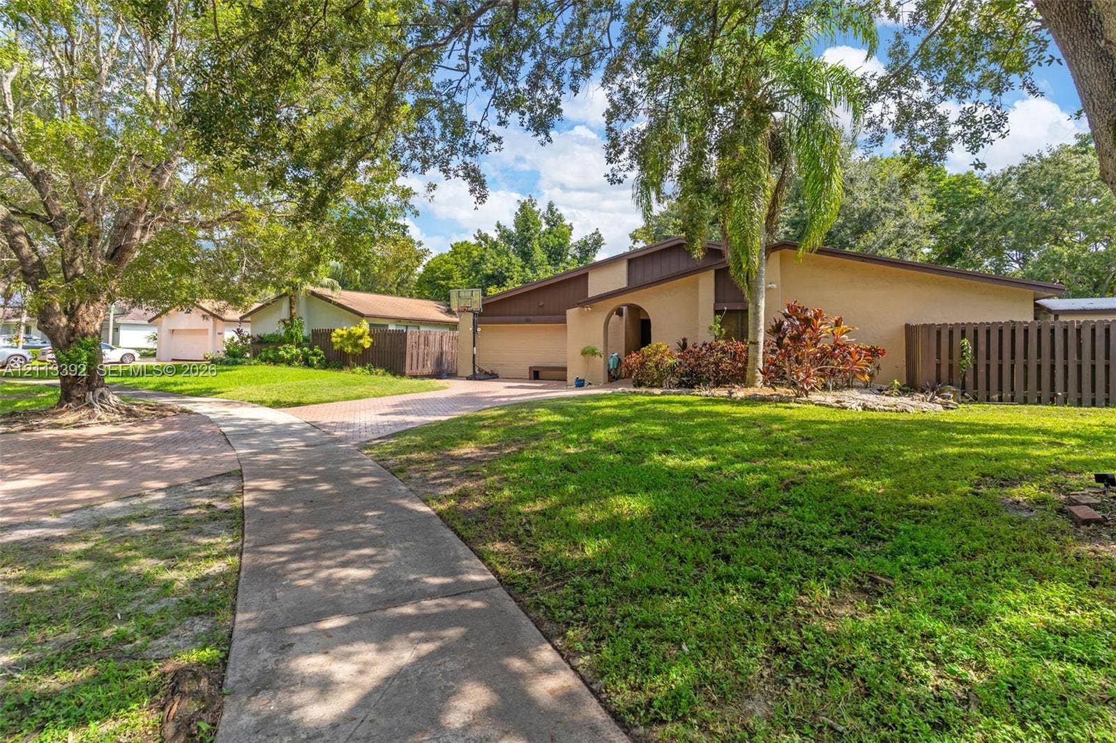 10705 SW 134th Court, Miami, FL 33186 Single-story residence featuring a stucco exterior, arched entryway, paved driveway, mature landscaping, and a fenced side yard