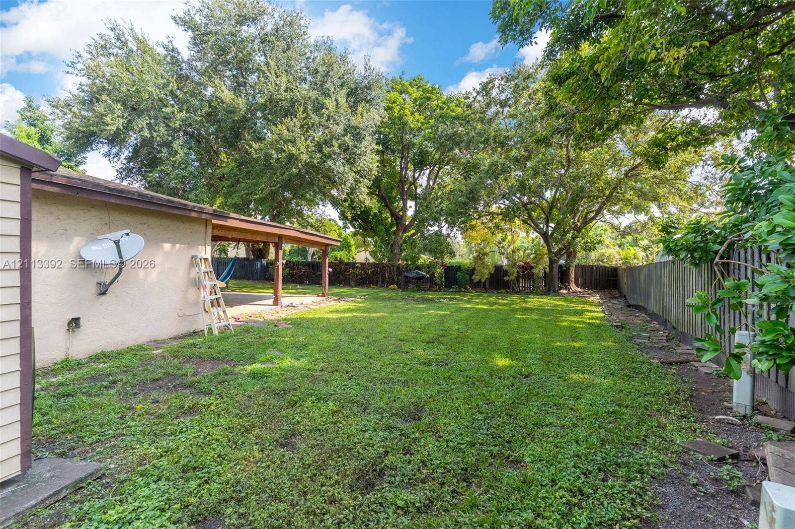 10705 SW 134th Court, Miami, FL 33186 Backyard featuring a covered patio, expansive lawn, mature trees, and wooden perimeter fencing