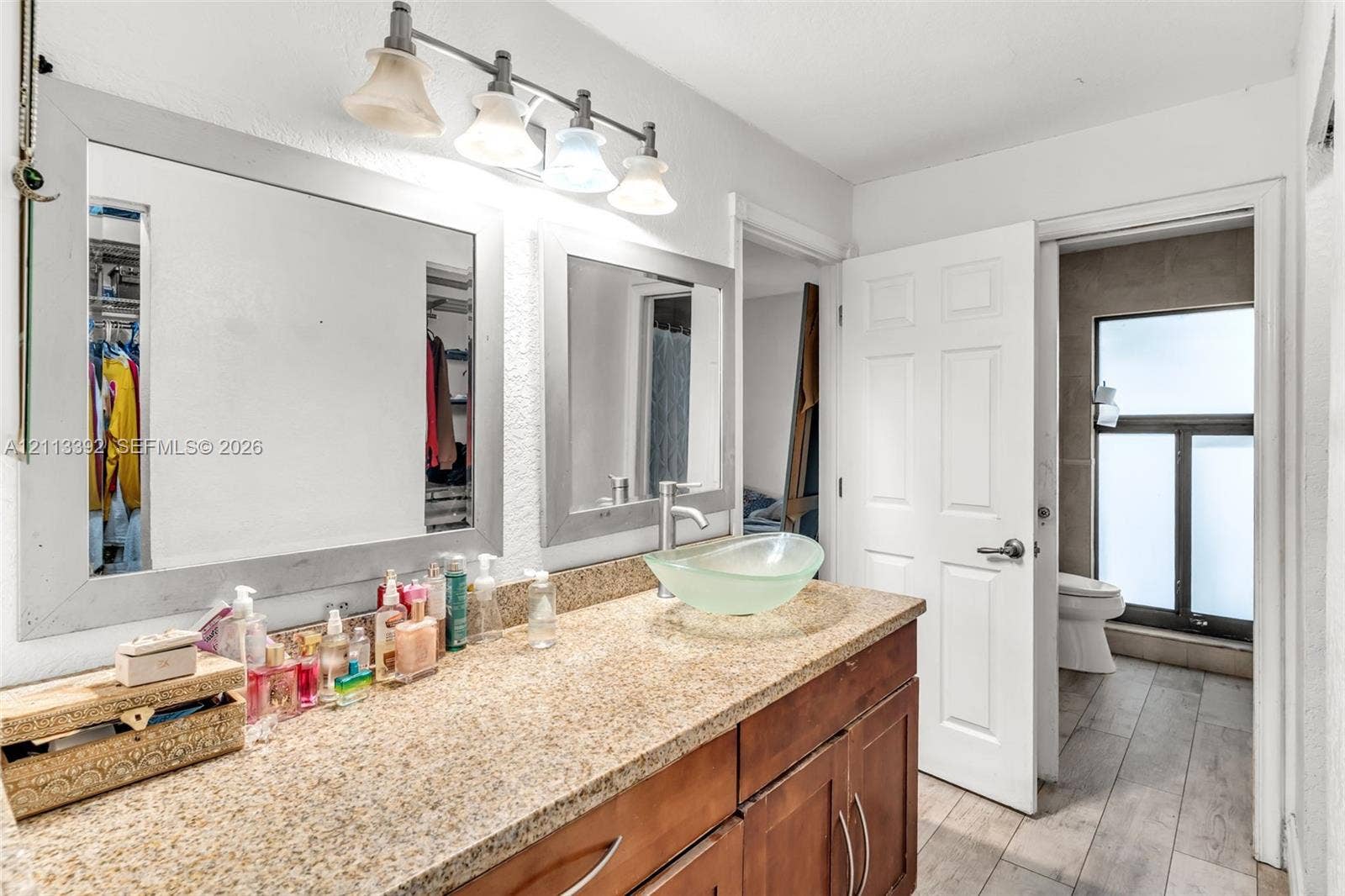 10705 SW 134th Court, Miami, FL 33186 Bathroom vanity featuring a speckled stone-finish countertop, dual wood-tone cabinets, glass vessel sink, and large framed wall mirrors