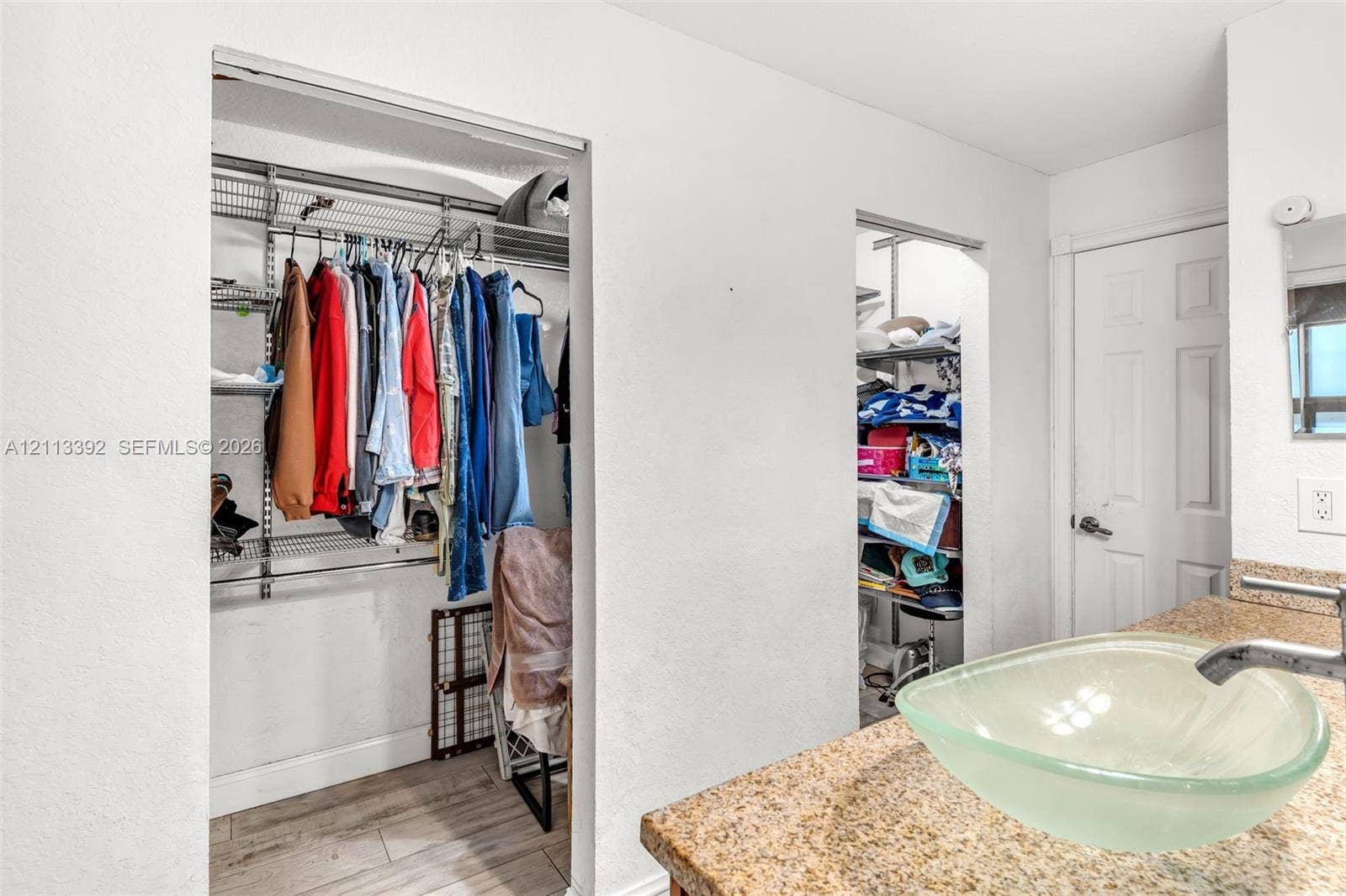 10705 SW 134th Court, Miami, FL 33186 Vanity featuring a stone countertop, glass vessel sink, and chrome faucet, accompanied by walk-in closets with integrated wire shelving and wood-finish flooring