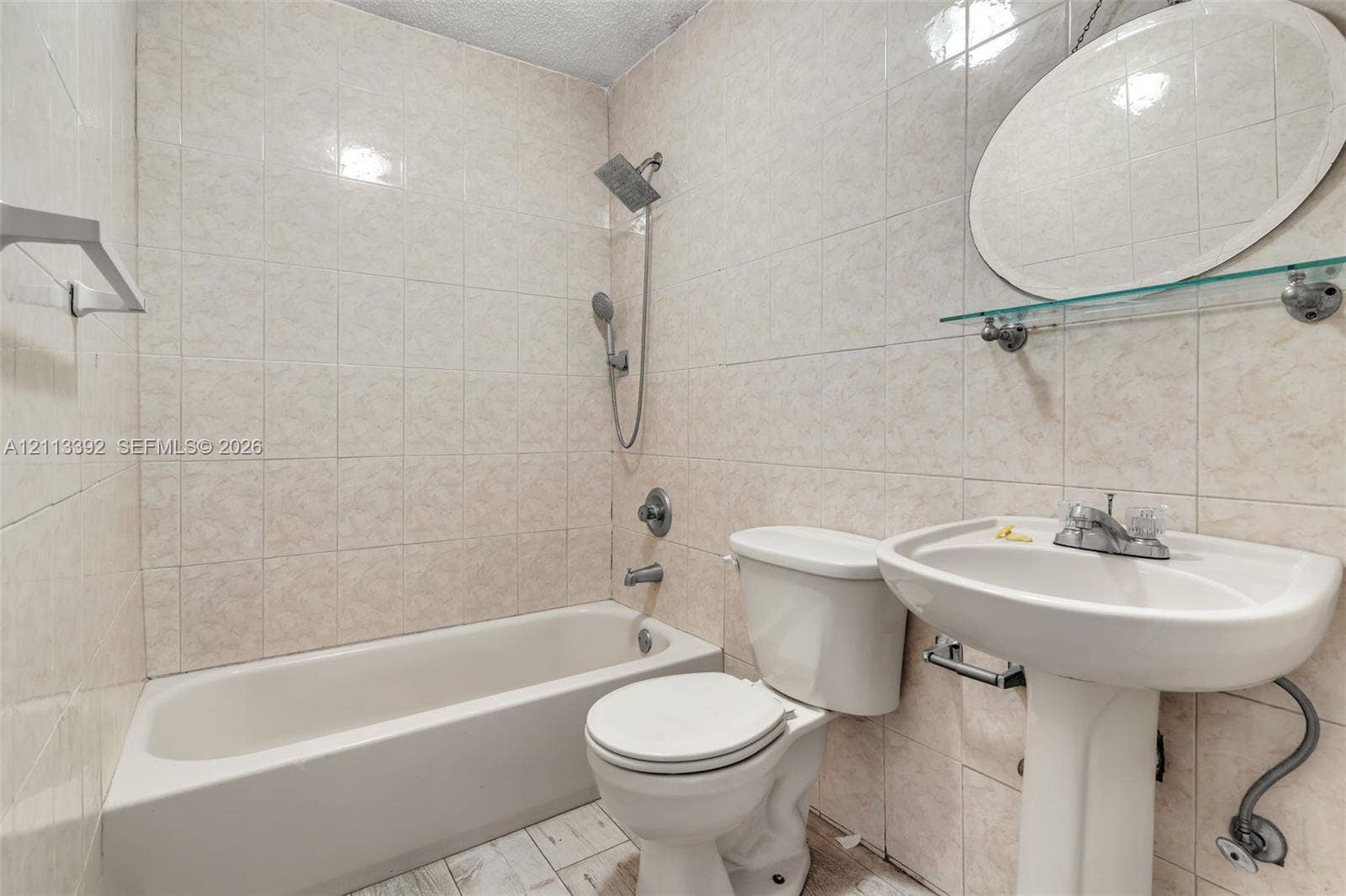 10705 SW 134th Court, Miami, FL 33186 Full bathroom featuring tile-surround tub with hand-held showerhead, pedestal sink, oval wall-mounted mirror, and glass shelving