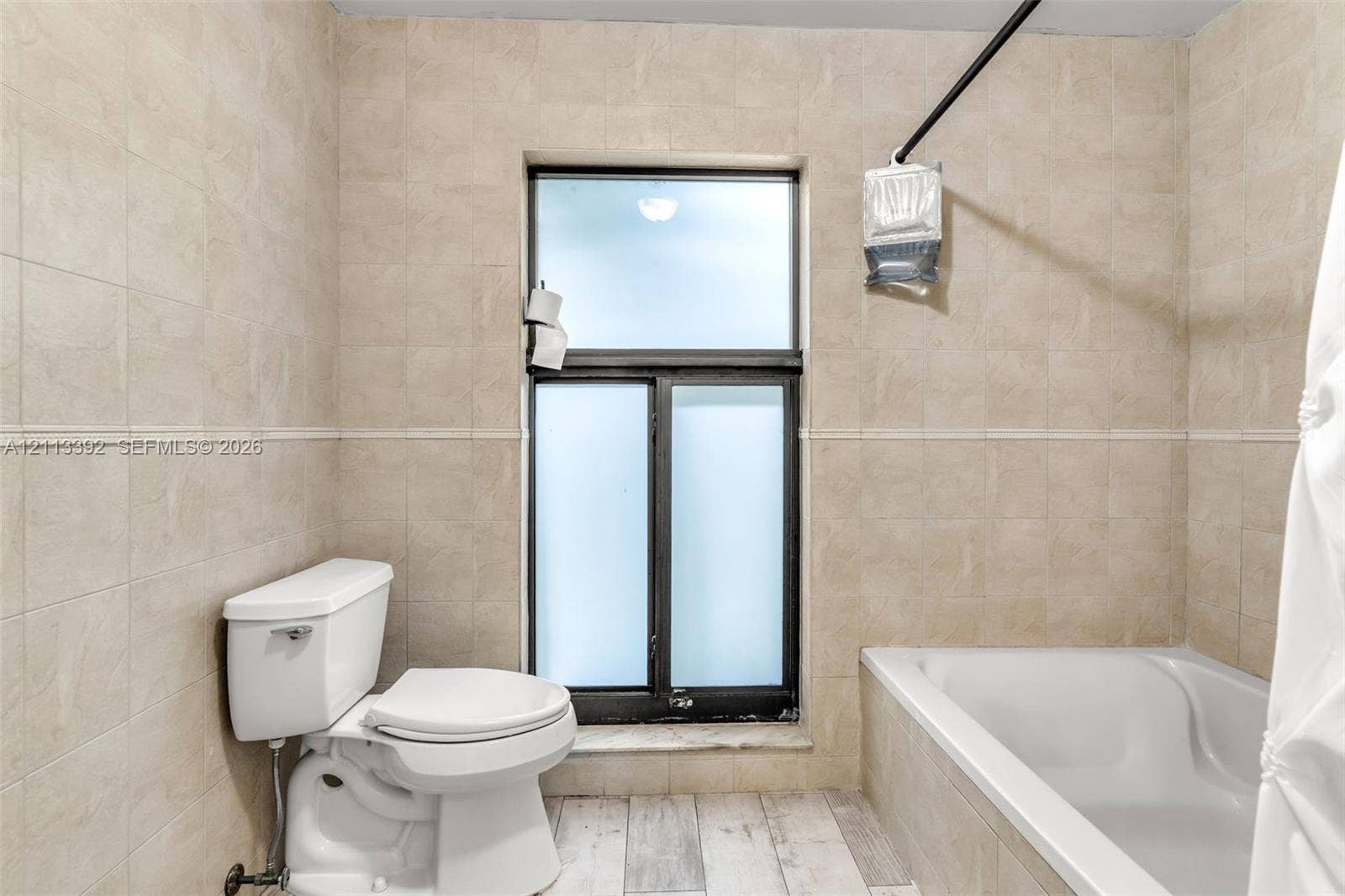 10705 SW 134th Court, Miami, FL 33186 Bathroom featuring neutral tile wall cladding, wood-finish flooring, a white soaking tub, and a window with frosted glass panes