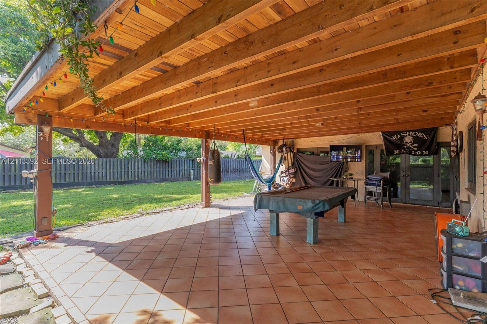 10705 SW 134th Court, Miami, FL 33186 Covered patio featuring a timber-frame ceiling, tile flooring, and vertical support posts, overlooking a lawn enclosed by a privacy fence