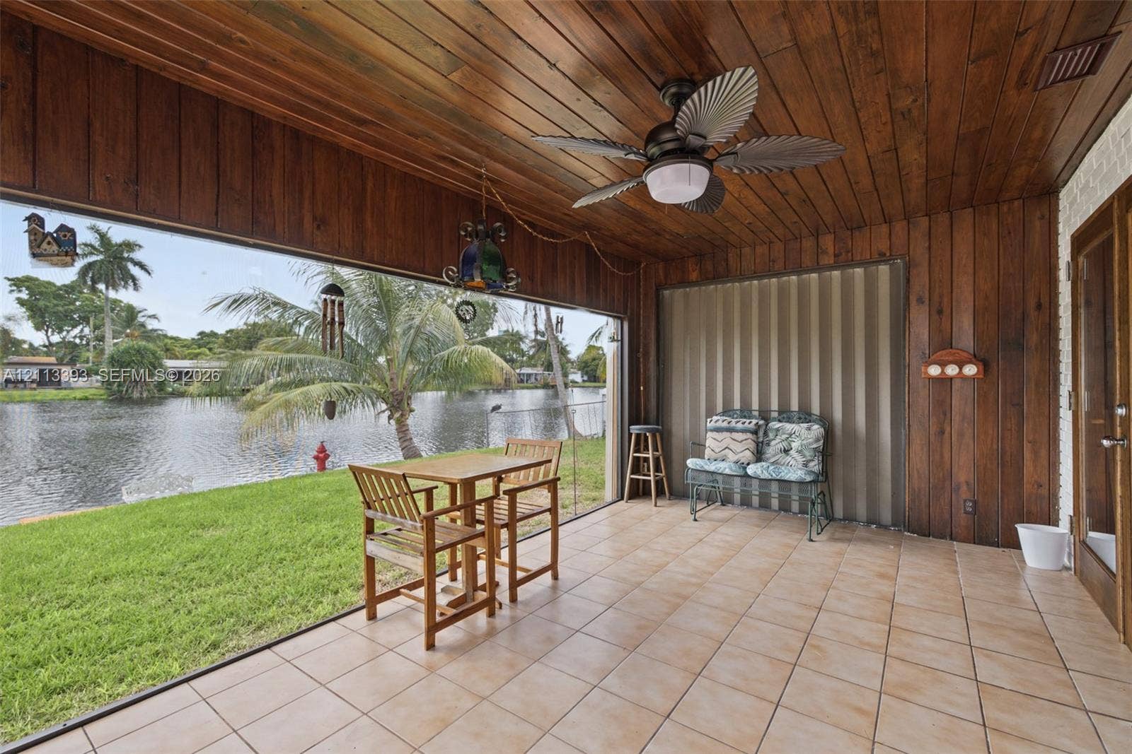 4136 SW 49th Street, Dania Beach, FL 33314 Screened patio featuring wood-paneled walls and ceiling, ceramic tile flooring, and a ceiling fan