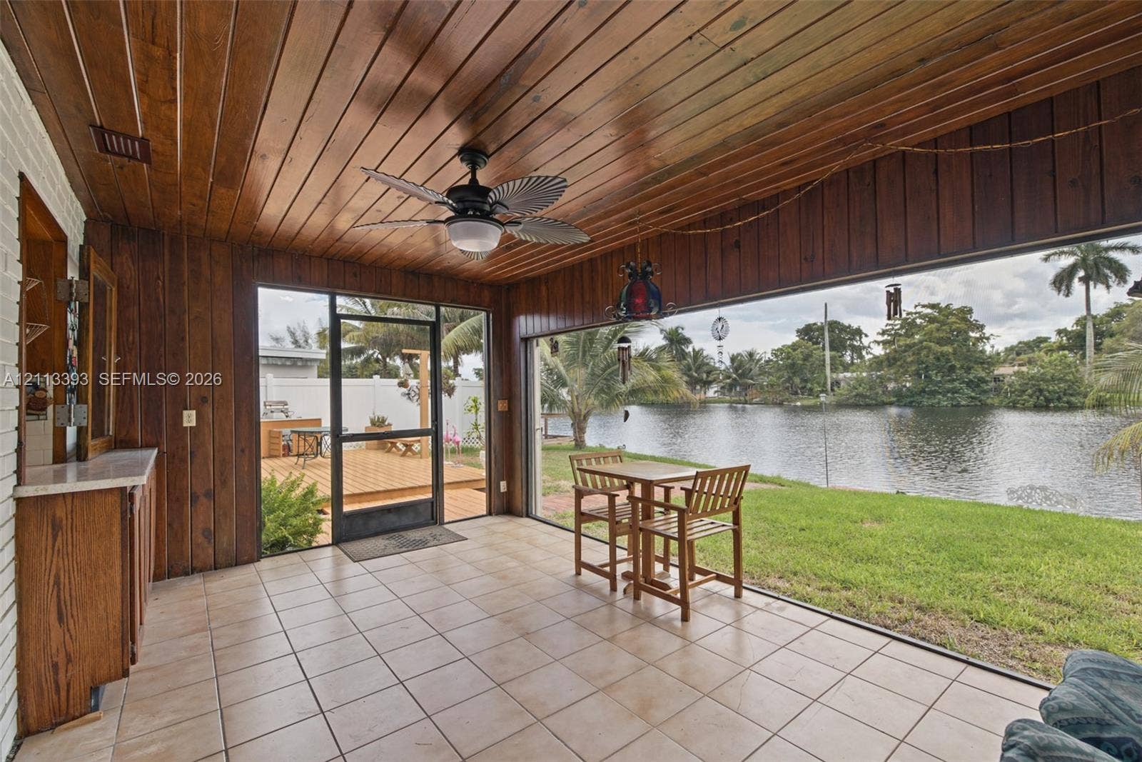 4136 SW 49th Street, Dania Beach, FL 33314 Screened-in porch featuring wood-paneled walls and ceiling, tile flooring, built-in cabinetry, and a ceiling fan