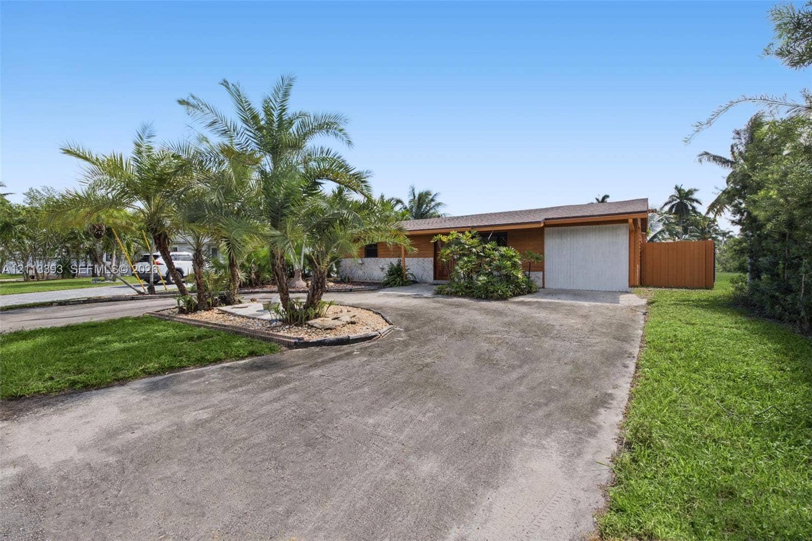 4136 SW 49th Street, Dania Beach, FL 33314 Single-story residence featuring stone masonry accents, a paved driveway, a one-car garage, established landscaping, and a wood privacy fence