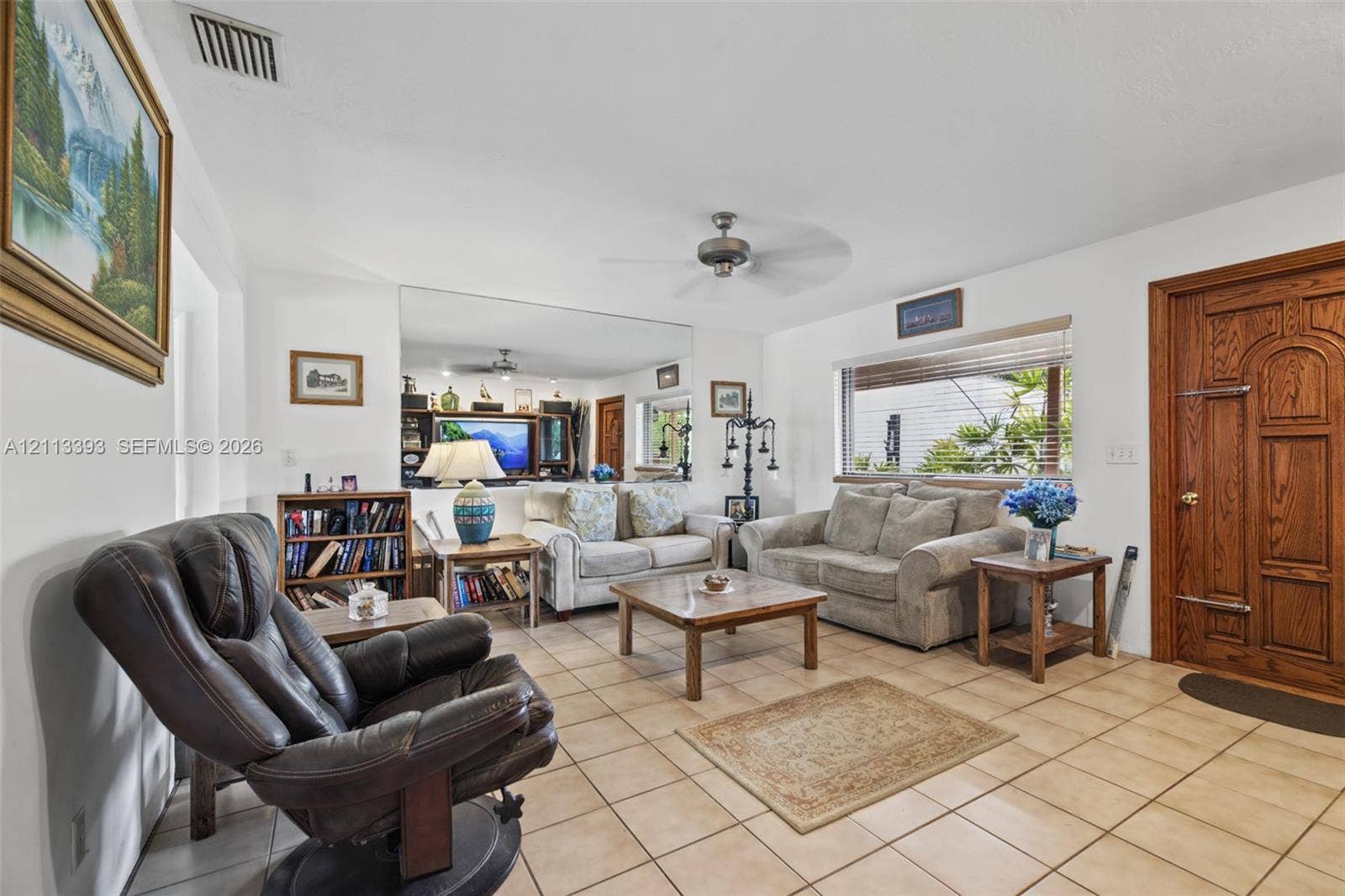 4136 SW 49th Street, Dania Beach, FL 33314 Living area featuring ceramic tile flooring, a large wall-mounted mirror, a ceiling fan, and a wood-finished entry door with ornate paneling