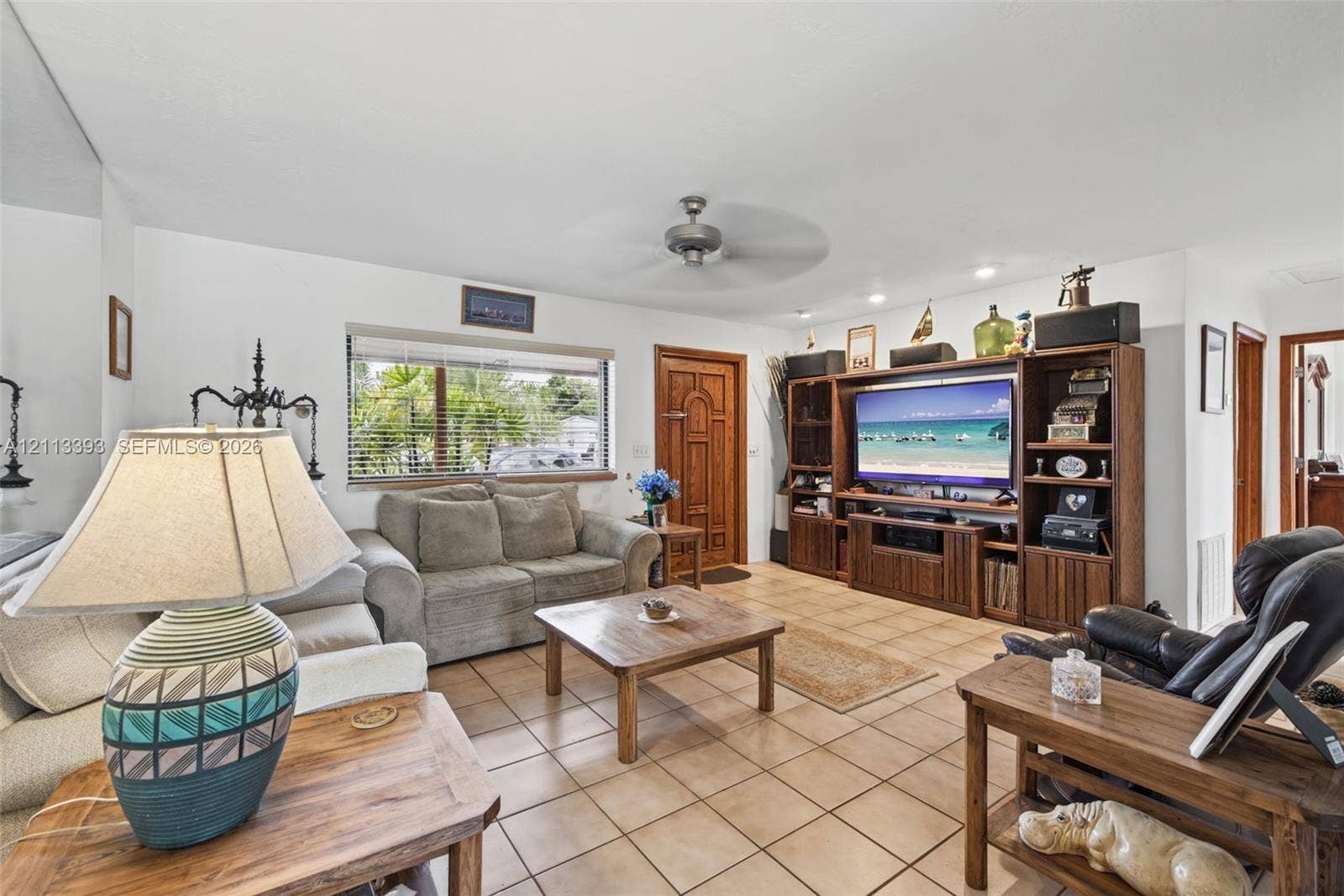 4136 SW 49th Street, Dania Beach, FL 33314 Living area featuring neutral tile flooring, built-in wooden media cabinetry, a solid wood front entry door, and a ceiling fan