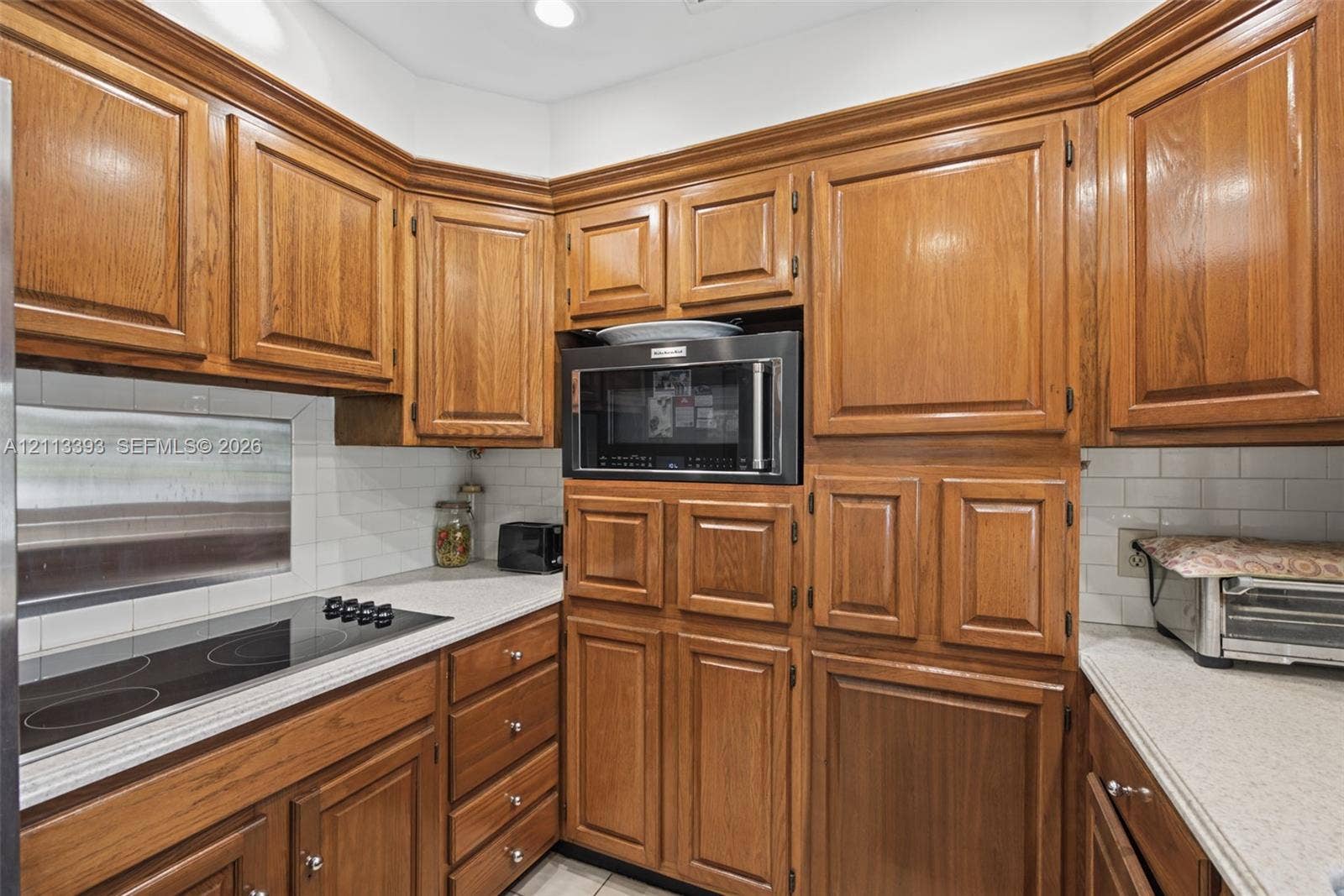 4136 SW 49th Street, Dania Beach, FL 33314 Kitchen featuring natural-finish wood cabinetry, a built-in microwave, a flush-mount electric cooktop, quartz countertops, and a white subway tile backsplash