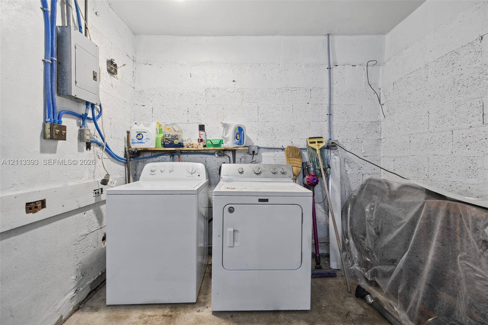 4136 SW 49th Street, Dania Beach, FL 33314 Utility area featuring exposed masonry walls, concrete flooring, built-in shelving, and dedicated laundry hookups with an electrical service panel