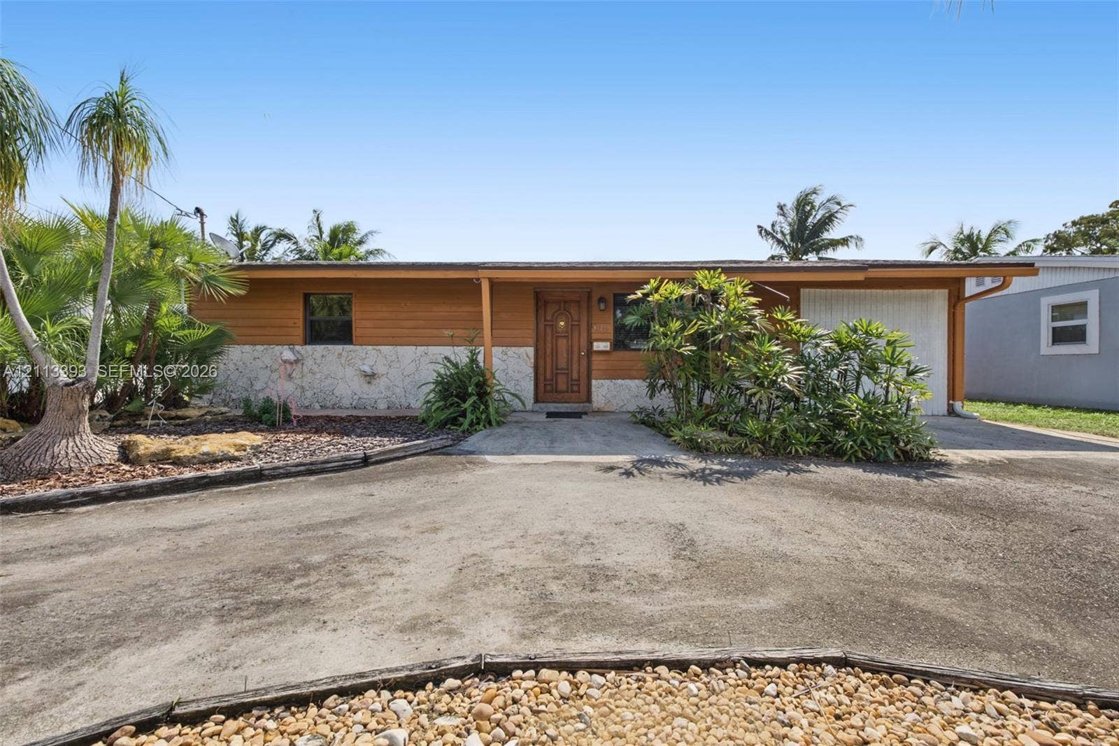 4136 SW 49th Street, Dania Beach, FL 33314 Single-story exterior featuring horizontal wood siding, natural stone veneer wainscoting, an attached garage, and a covered entryway