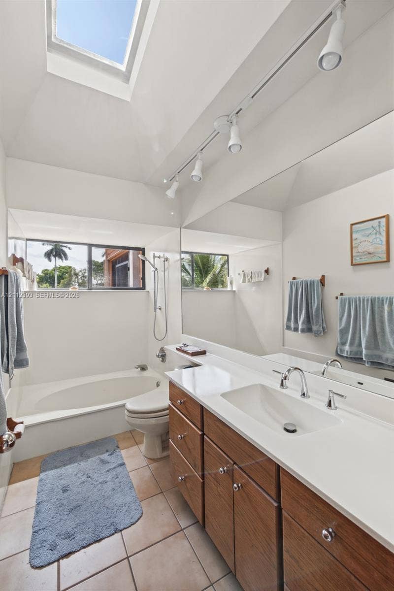 4136 SW 49th Street, Dania Beach, FL 33314 Bathroom featuring a skylight, wood-finish vanity with a solid-surface countertop, integrated basin, and track lighting