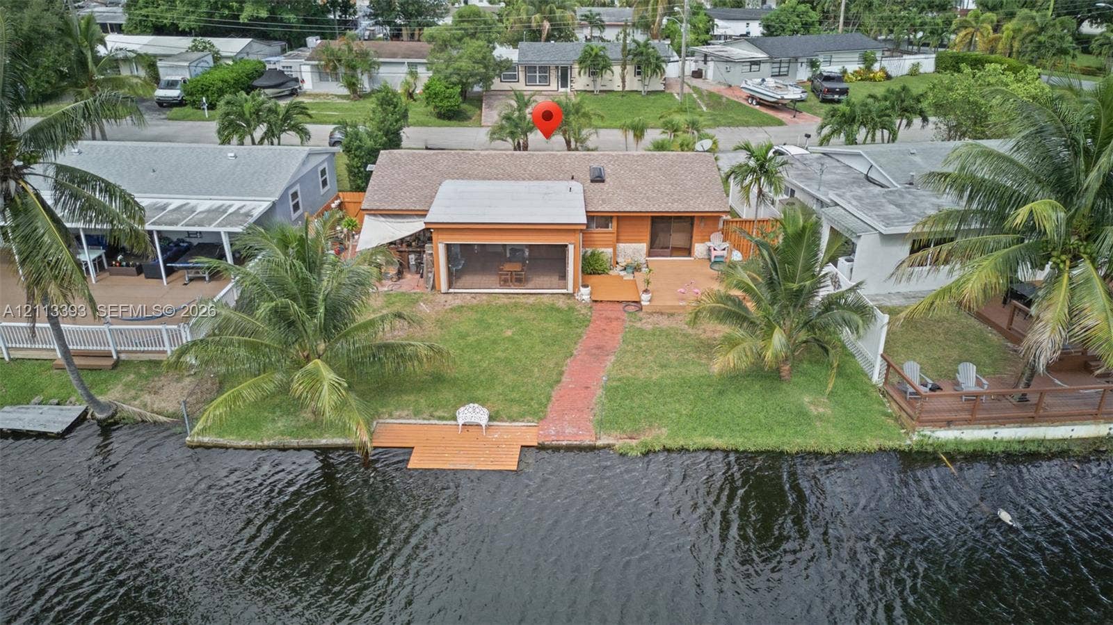 4136 SW 49th Street, Dania Beach, FL 33314 Waterfront residence featuring a screened-in lanai, wood-finish decking, a paved walkway, and direct water access with a private dock