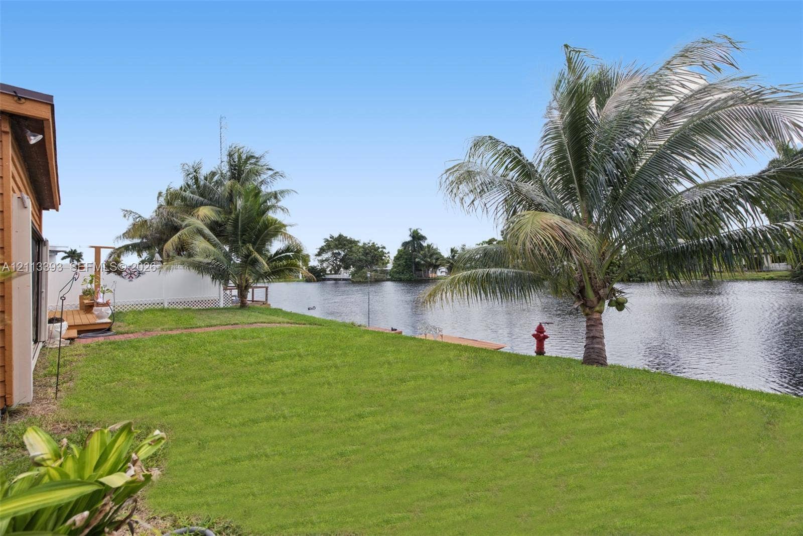 4136 SW 49th Street, Dania Beach, FL 33314 Waterfront lot featuring a grass lawn, established palm trees, wooden decking, and a privacy fence
