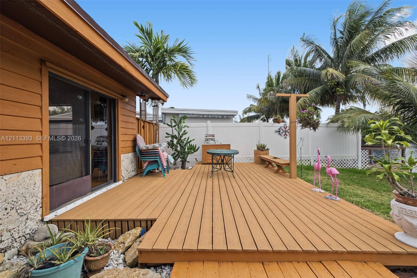4136 SW 49th Street, Dania Beach, FL 33314 Raised wood-finish deck with sliding glass door access, stone veneer foundation, and white vinyl privacy fencing