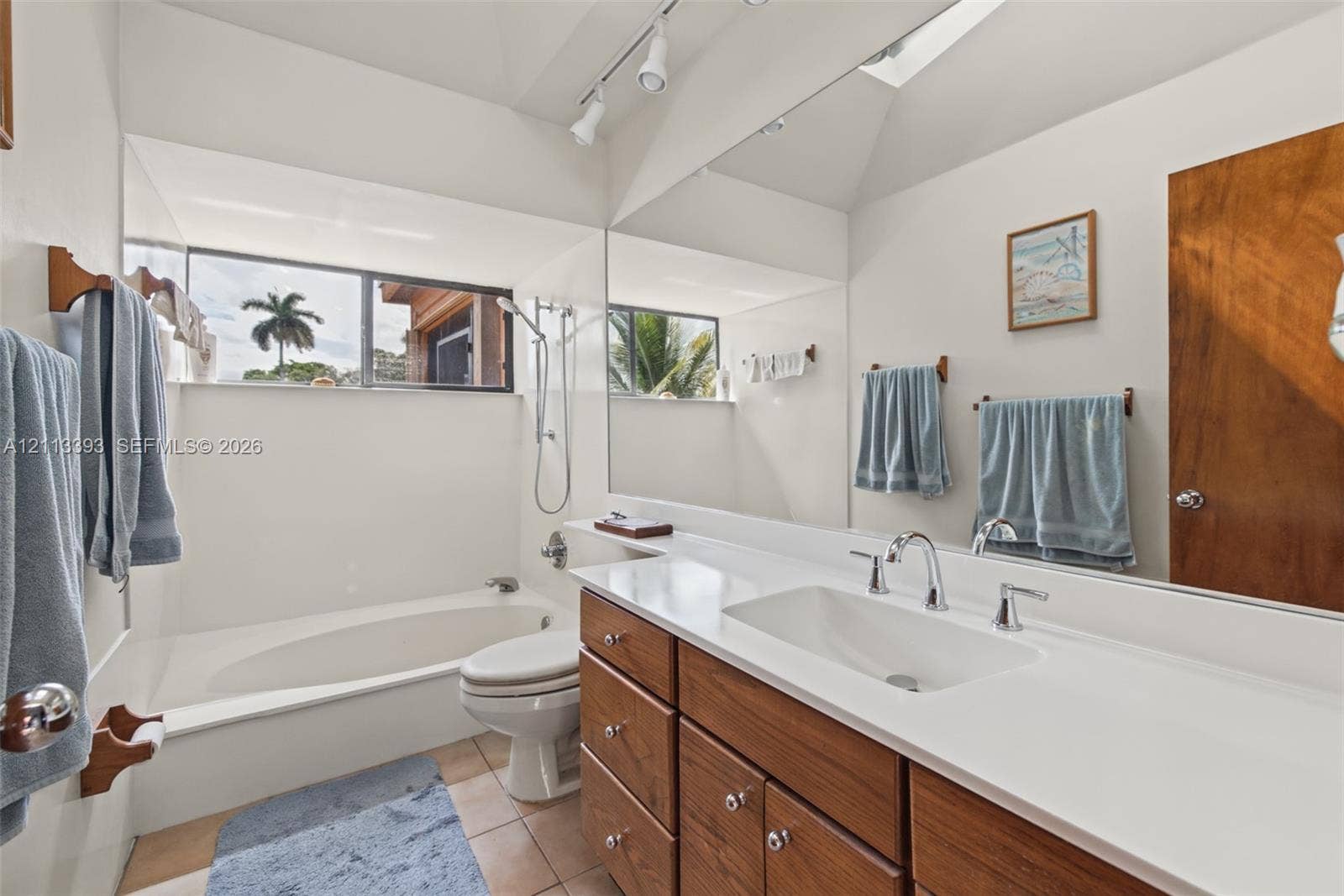 4136 SW 49th Street, Dania Beach, FL 33314 Bathroom featuring wood-finish cabinetry, a large wall-to-wall vanity mirror, a rectangular drop-in sink, and a porcelain soaking tub with a handheld shower attachment