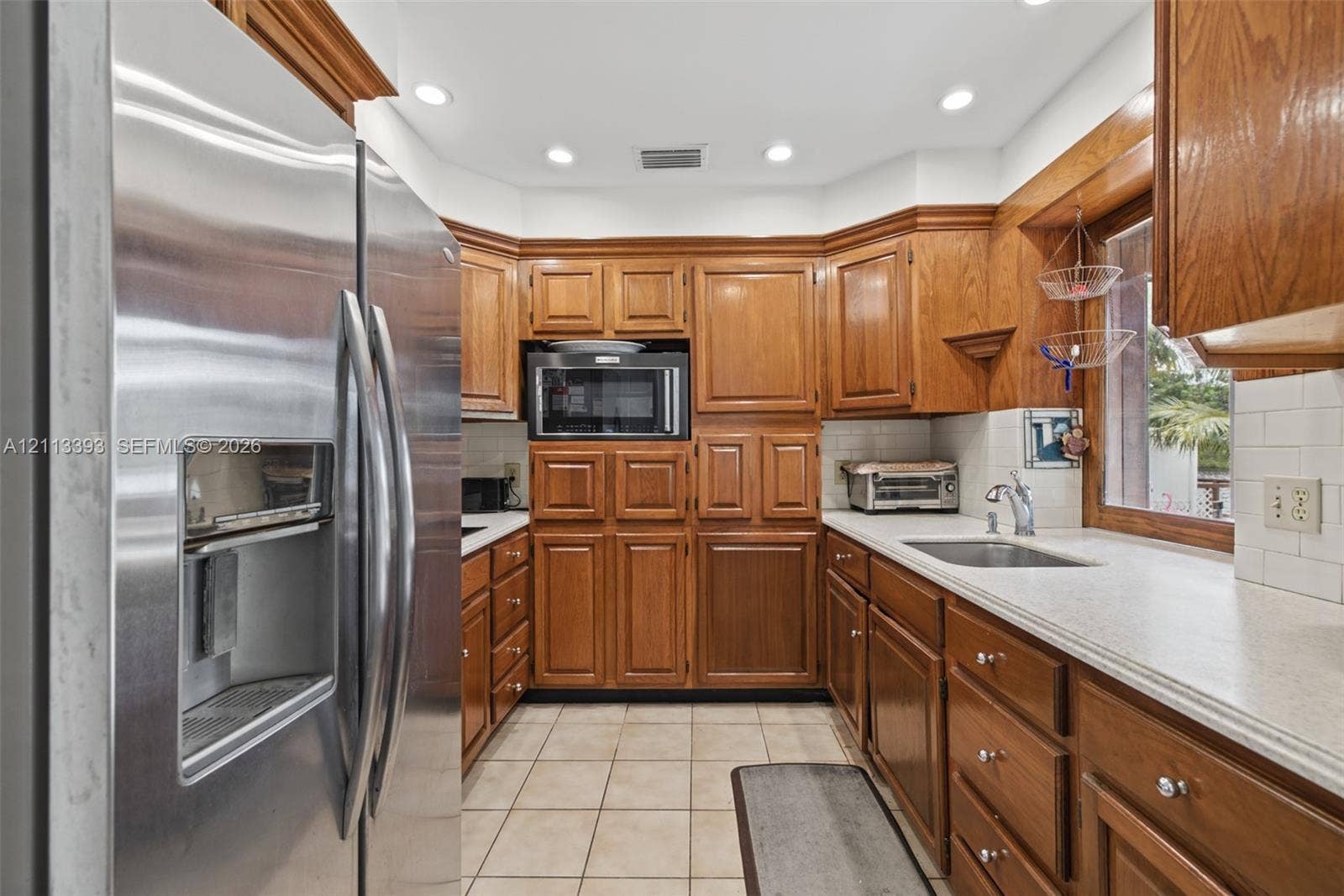 4136 SW 49th Street, Dania Beach, FL 33314 Kitchen featuring custom wood cabinetry, stainless steel refrigerator, built-in microwave, stone-finish countertops, and subway tile backsplash