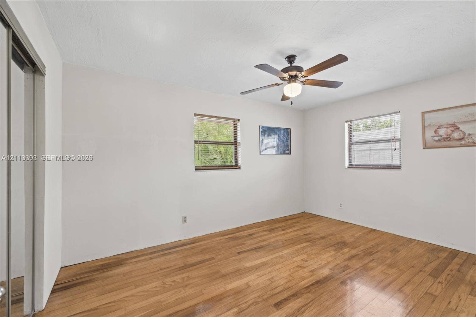 4136 SW 49th Street, Dania Beach, FL 33314 Room featuring wood-finish flooring, two windows with horizontal blinds, a ceiling-mounted fan with integrated light, and a sliding mirrored closet door
