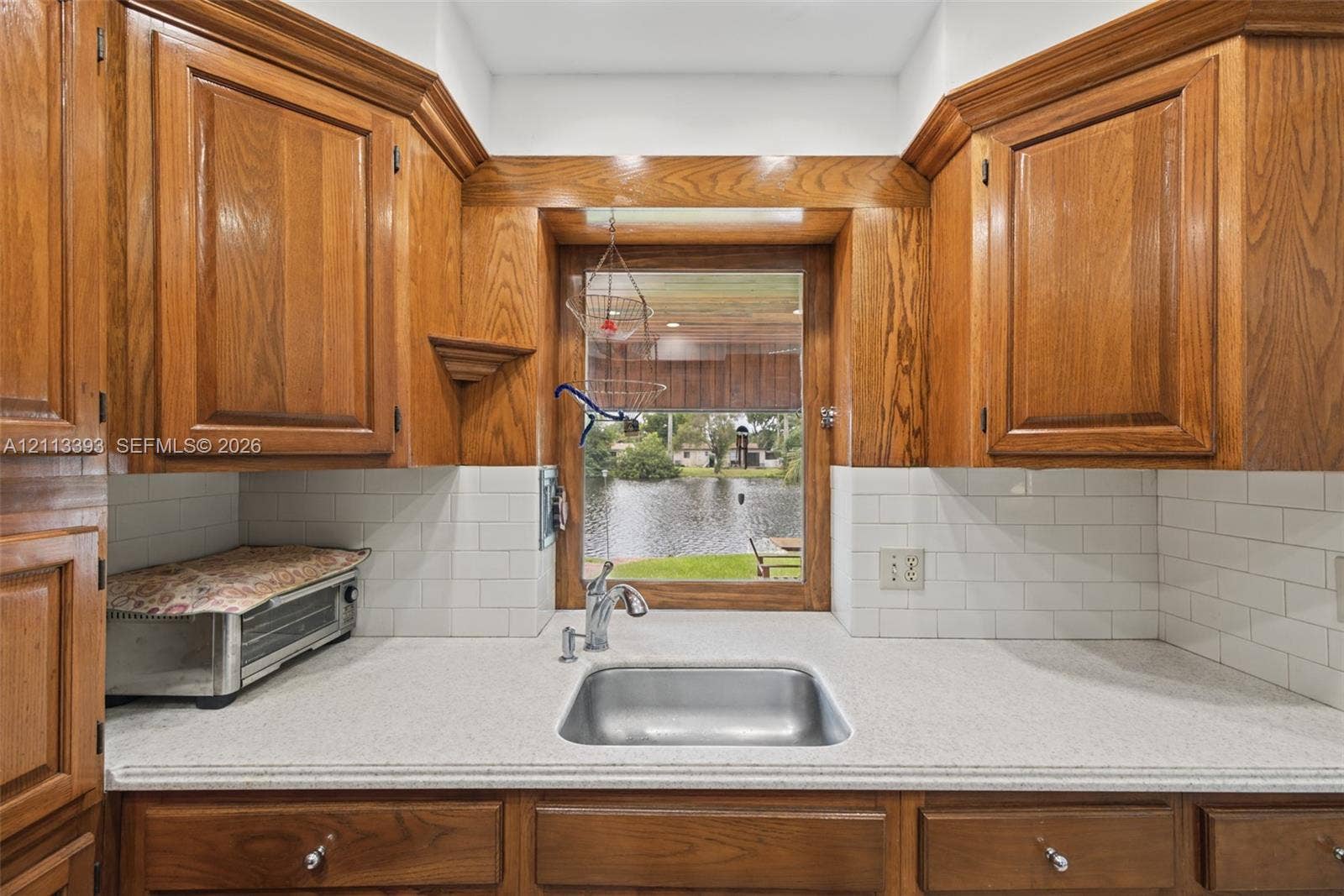 4136 SW 49th Street, Dania Beach, FL 33314 Kitchen featuring custom wood cabinetry, a stainless steel undermount sink with a gooseneck faucet, light-toned solid surface countertops, and white subway tile backsplash