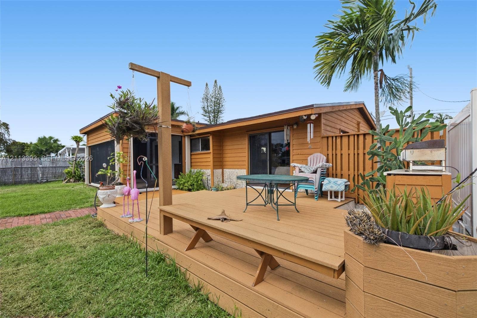 4136 SW 49th Street, Dania Beach, FL 33314 Elevated wood deck with a built-in bench, wood-sided exterior, sliding glass doors, and a wood privacy fence