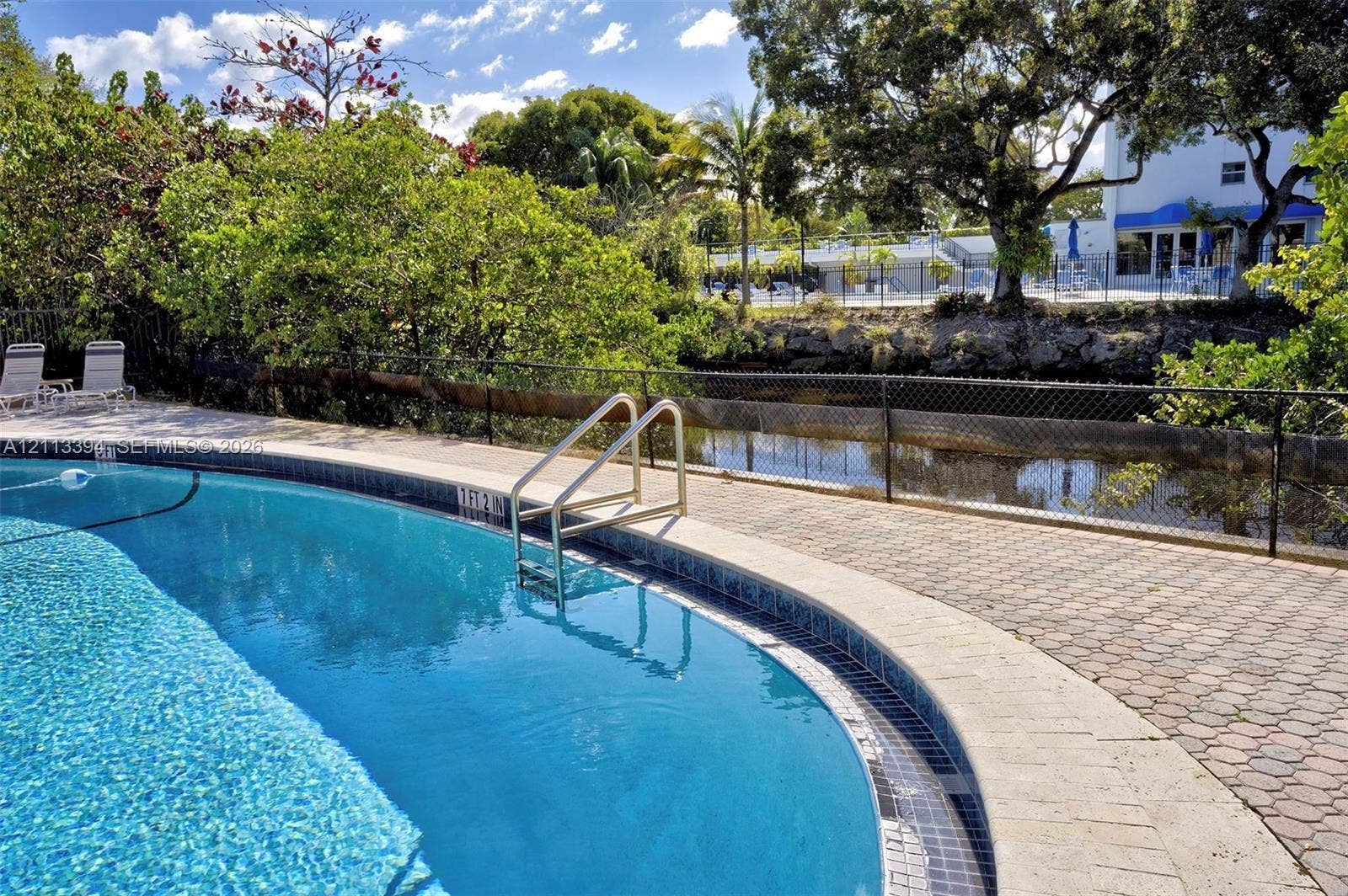 124 NE 19th Court, #108B, Wilton Manors, FL 33305 Curved in-ground swimming pool with metal handrails, stone-paver pool deck, and perimeter fencing
