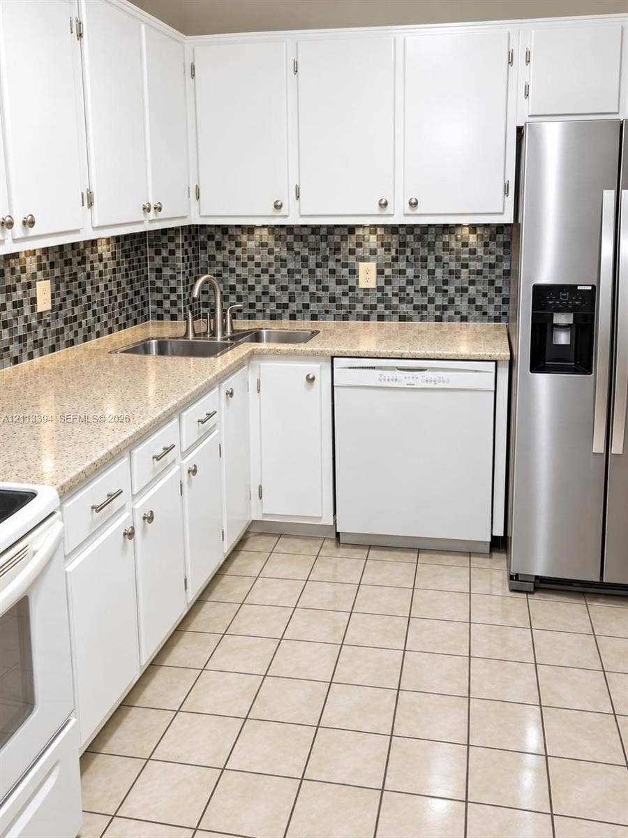 124 NE 19th Court, #108B, Wilton Manors, FL 33305 Kitchen featuring white cabinetry, solid-surface countertops, a mosaic tile backsplash, stainless steel refrigerator, and ceramic tile flooring