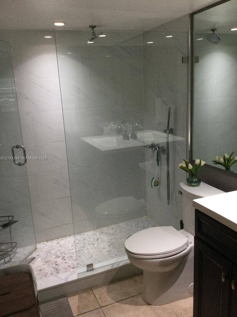 124 NE 19th Court, #108B, Wilton Manors, FL 33305 Walk-in shower featuring a frameless glass enclosure, pebble-stone flooring, large-format tile surround, and recessed ceiling lighting